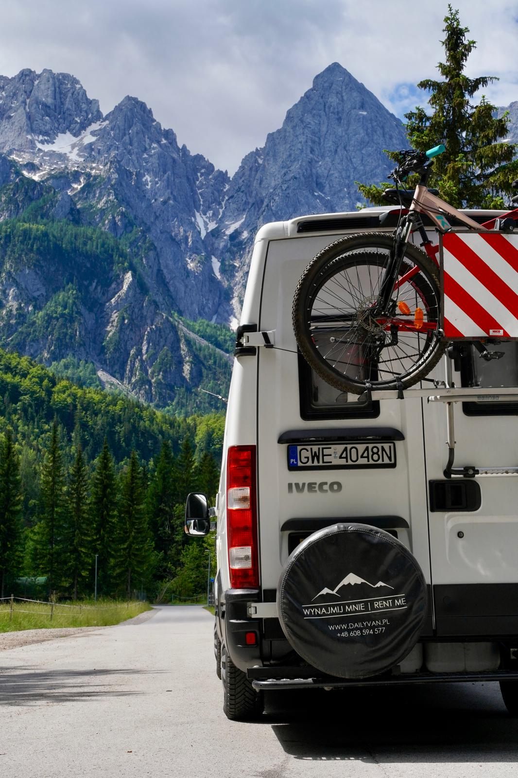 Iveco Daily z rowerem na bagażniku i kołem zapasowym, w tle góry